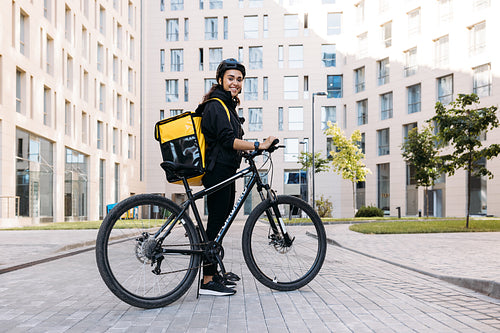 Smiling courier girl with bicycle, wearing a delivery thermal backpack looking at camera