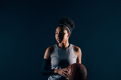 Female basketball player in sportswear over black backdrop. Young professional basketball player with ball, wearing team attire.