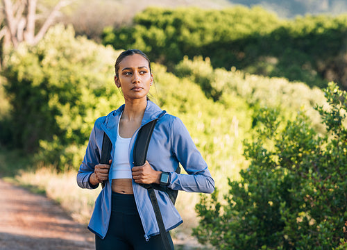 Portrait of a female hiker at sunset. Woman with a backpack wearing sportswear standing outdoors.