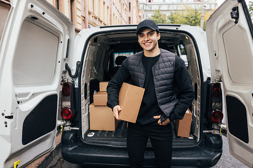 Portrait of a smiling courier holding a cardboard box while stan