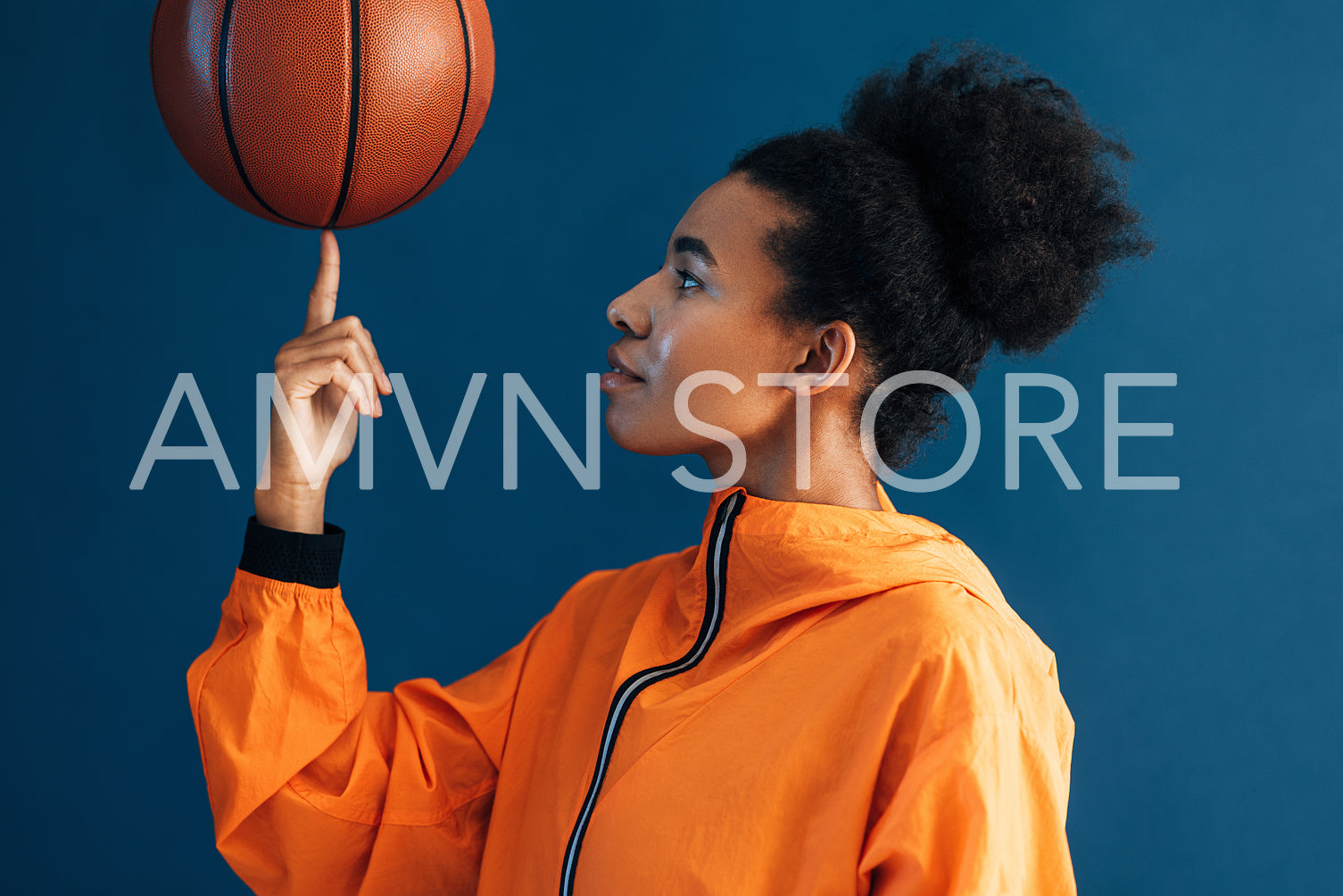 Side view of young woman with curly hair holding basketball on finger. Studio shot of female basketball player posing in studio.