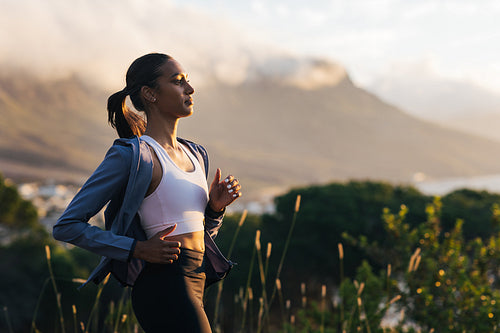 Side view of a young slim female jogging outdoors at a stunning sunset