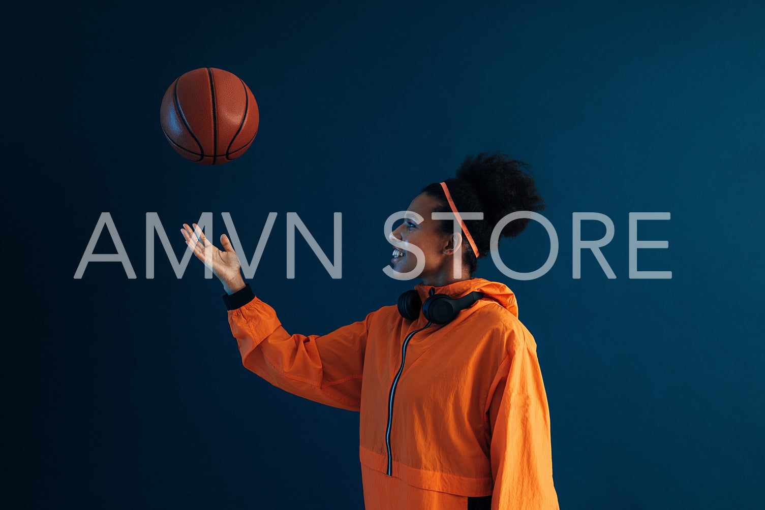 Young basketball woman tosses a ball in studio over a blue backdrop. Female in orange sportswear with basketball in the studio.