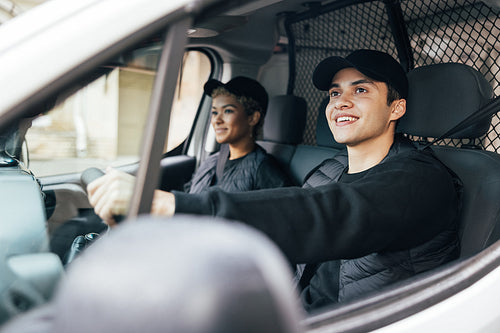 Two delivery coworkers sitting in van. Smiling courier driving a