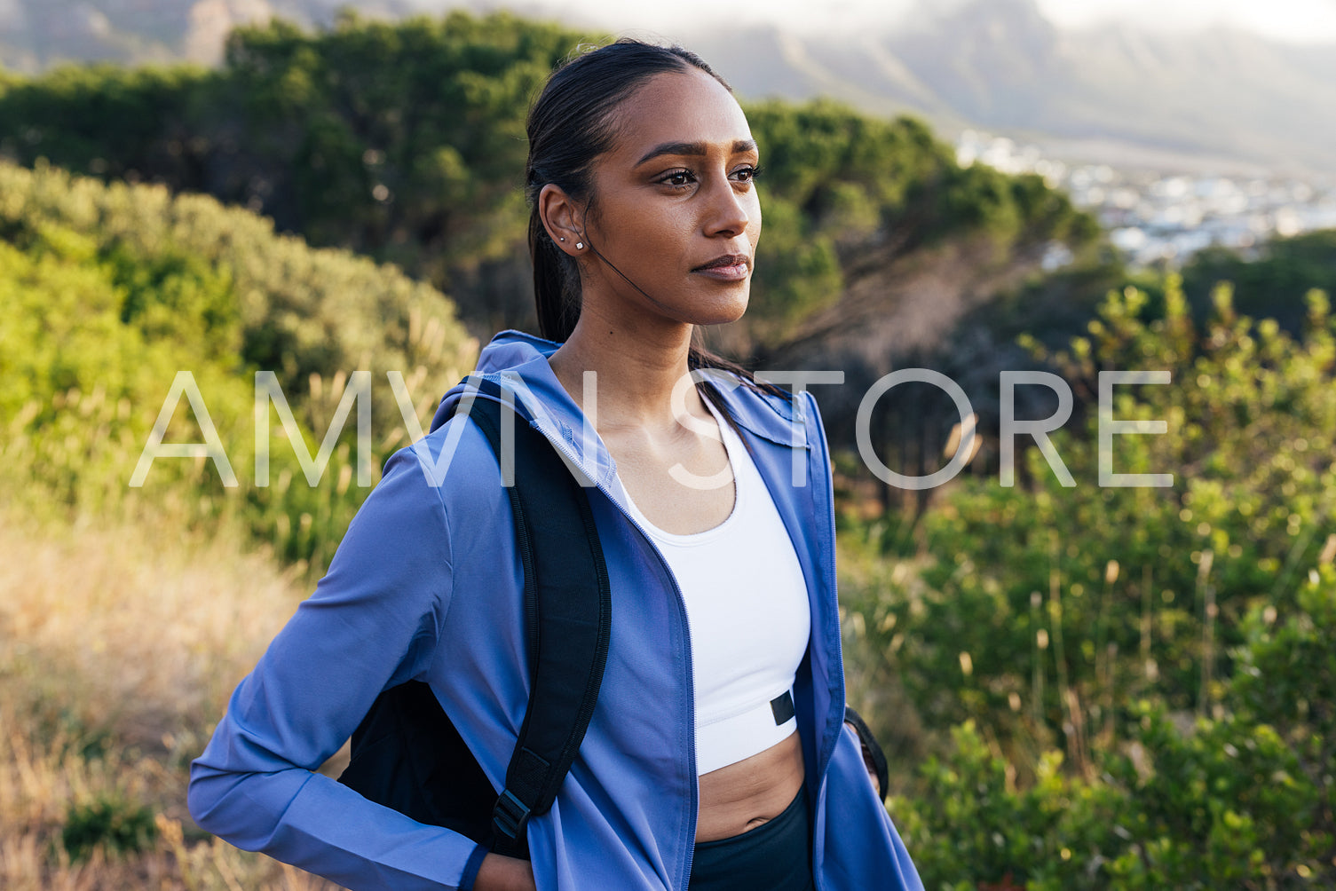 Portrait of young female in sportswear with backpack standing outdoors at sunset 