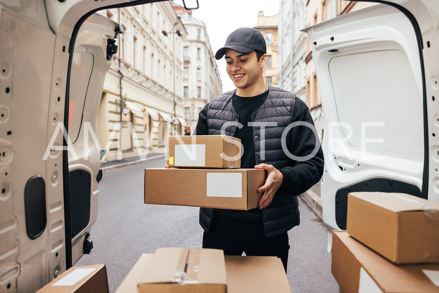 Smiling man courier in uniform standing at car trunk holding box