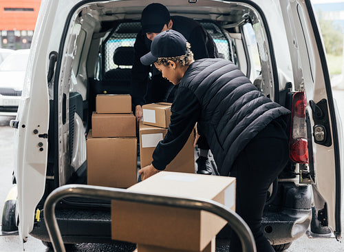 Woman courier loads cardboard boxes from a cart into a car worki