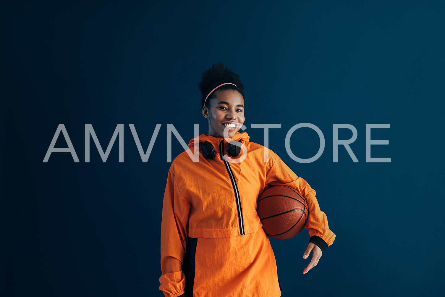 Young woman in orange fitness clothes with a basketball over a blue background