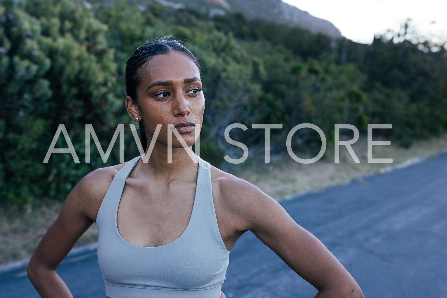 Young and confident woman athlete standing on abandoned road and looking away, taking a break during outdoor workout 