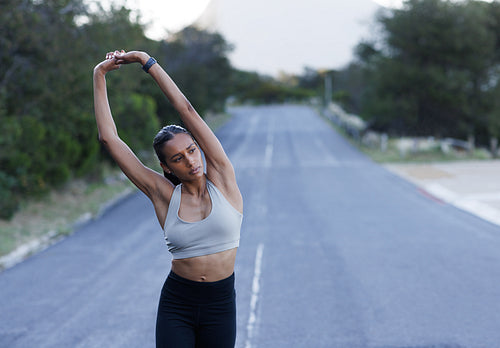 Young slim woman in fitness wear warming up hands while walking on an abandoned road