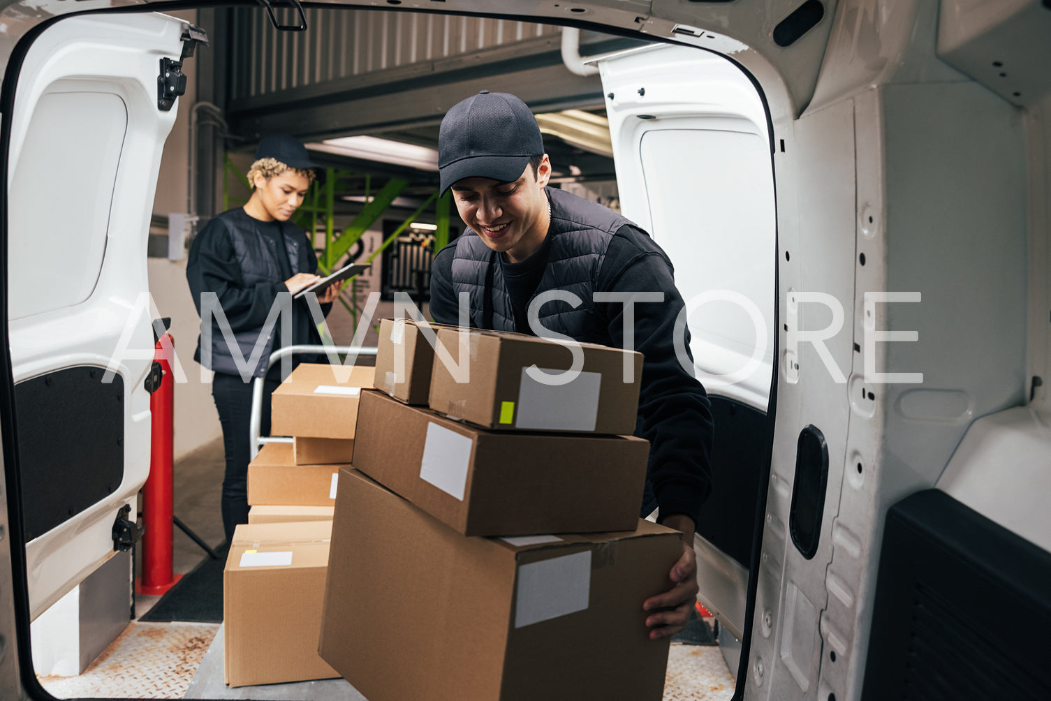 Smiling male courier loads cardboard boxes from a cart into the