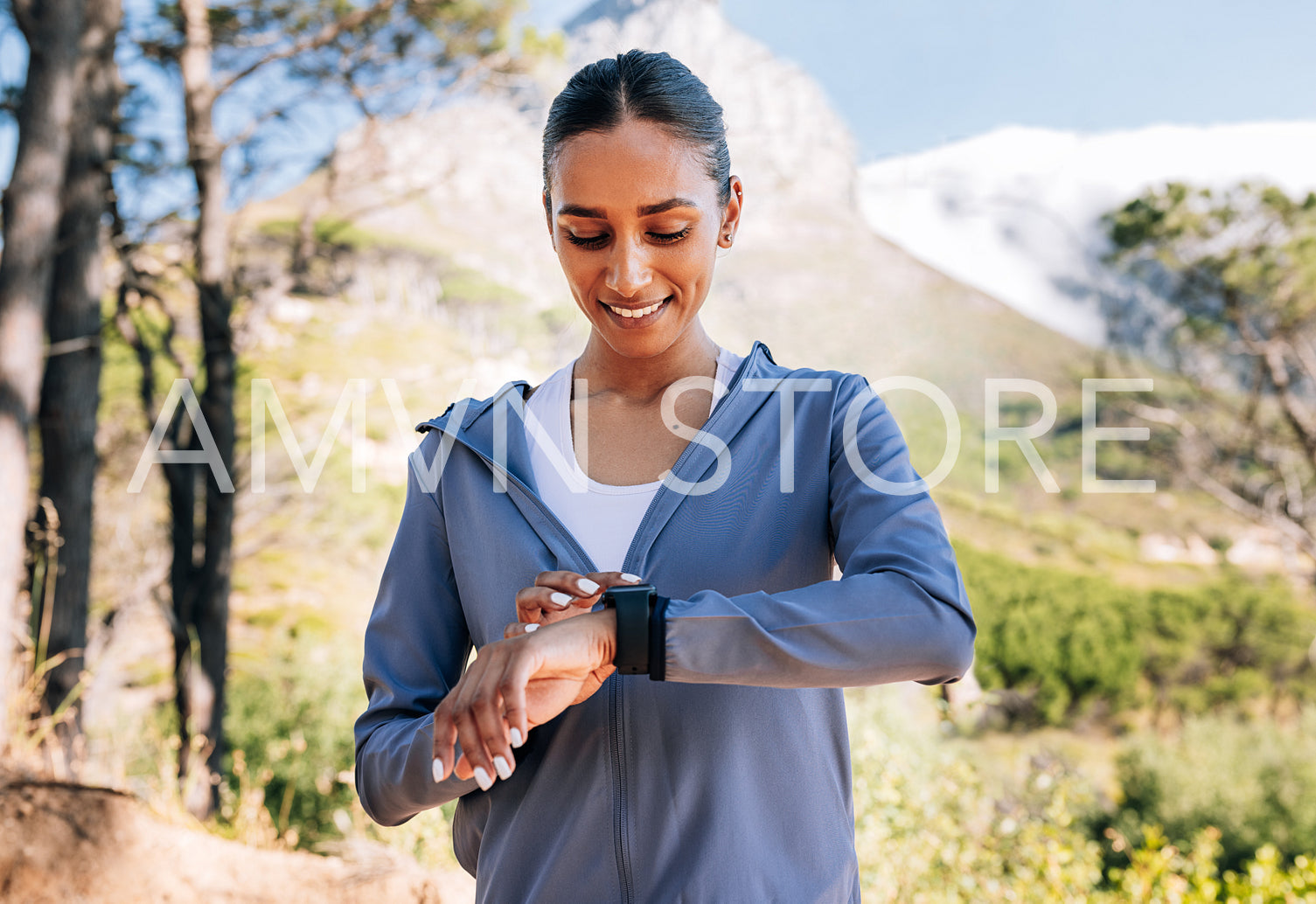 Cheerful woman checking her smartwatches after a workout in a natural park. Smiling slim female checking pulse on a fitness tracker.