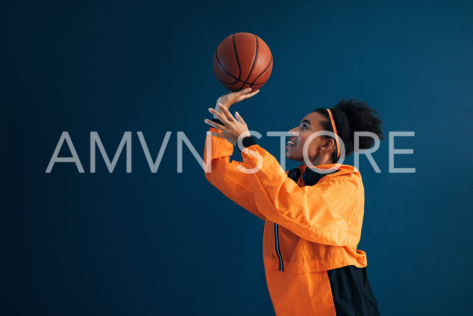 Side view of smiling basketball player in orange fitness attire practicing throwing over blue background