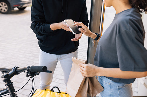 Woman receiving food delivery at the doorway. Midsection of an unrecognizable woman making a sign on a smartphone.