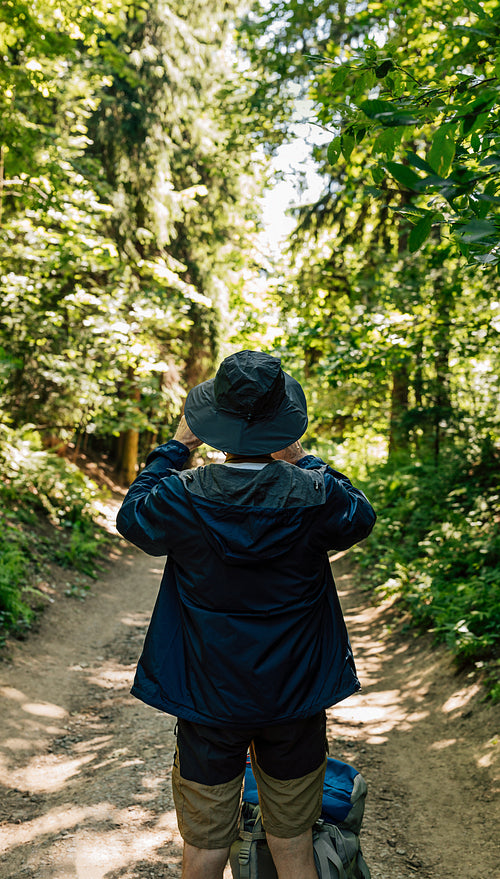 Back view of male in hat and hiking clothes taking photographs during trekking