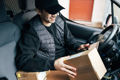 Smiling male courier in uniform sitting on driver's seat holding