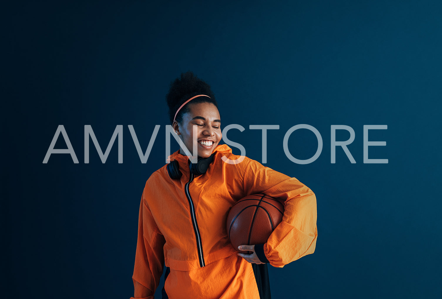 Young cheerful female with curly hair holding a basketball with eyes closed