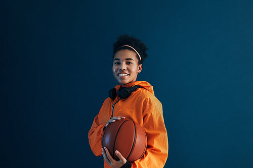 Smiling female with basketball wearing orange sportswear and looking at camera. Professional basketball player posing in studio.