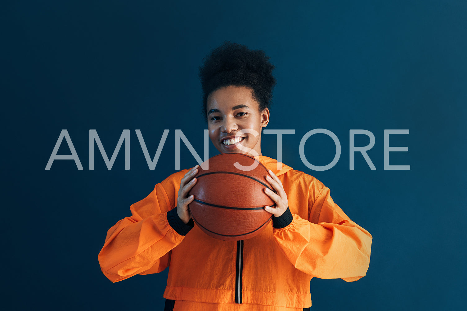 Happy basketball player with a ball over the blue backdrop. Smiling woman with a basketball looking at the camera in studio.