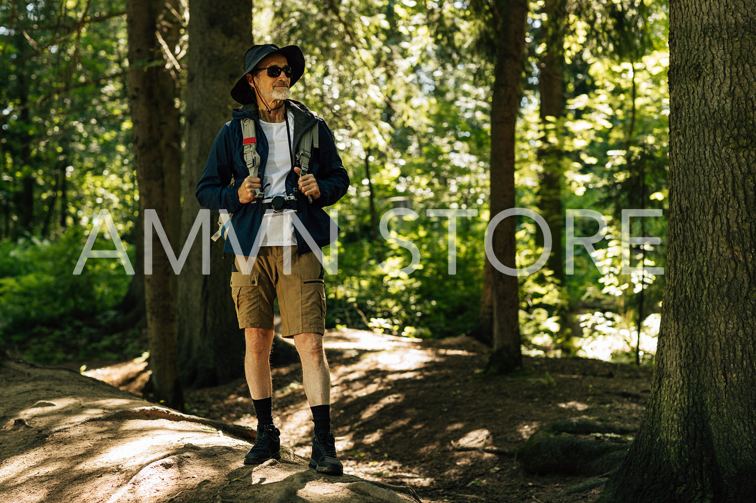 Confident senior tourist standing with backpack in forest and looking away