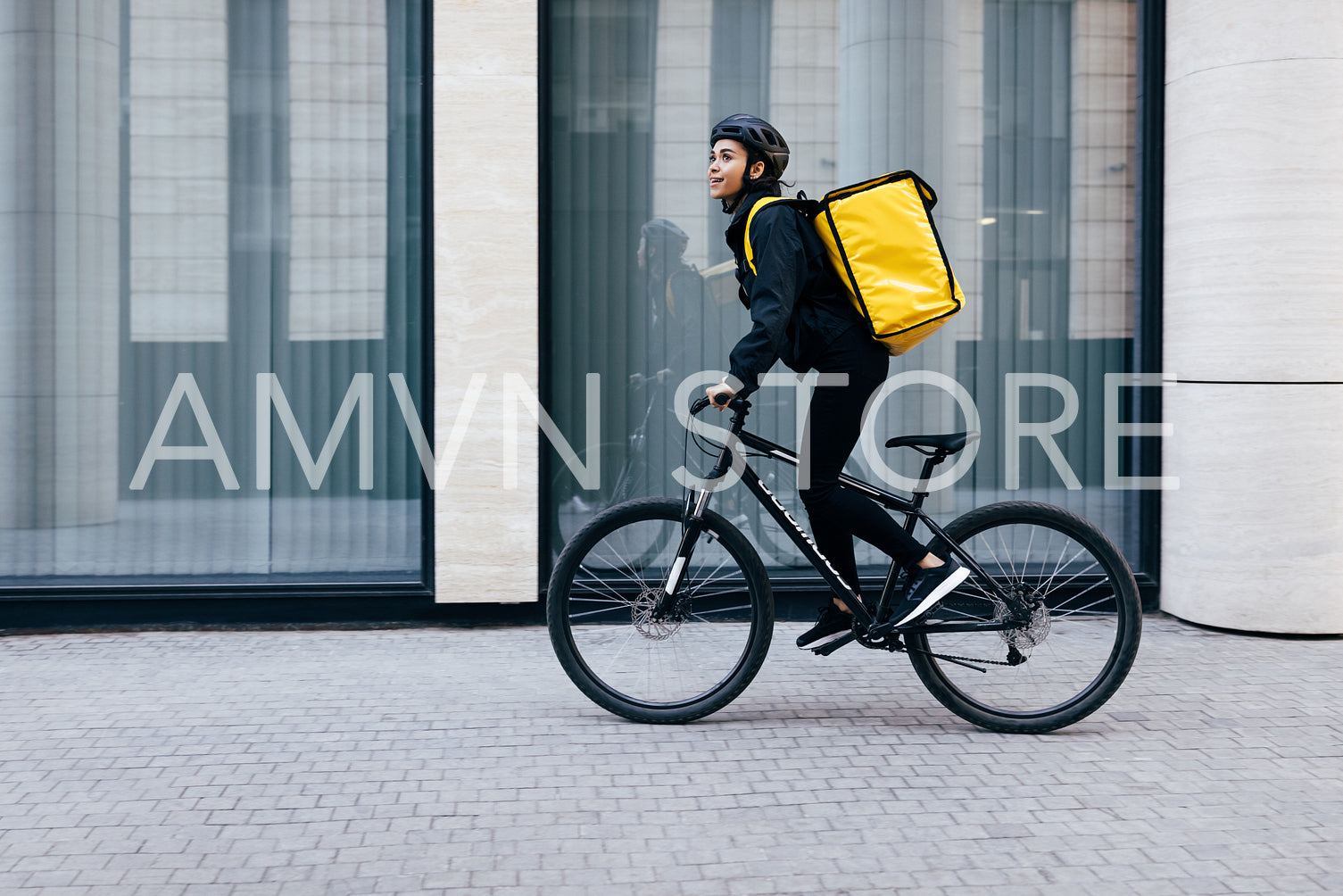 Side view of a young woman riding her bike in the city. Courier with a thermal backpack in her way to deliver food to a customer.