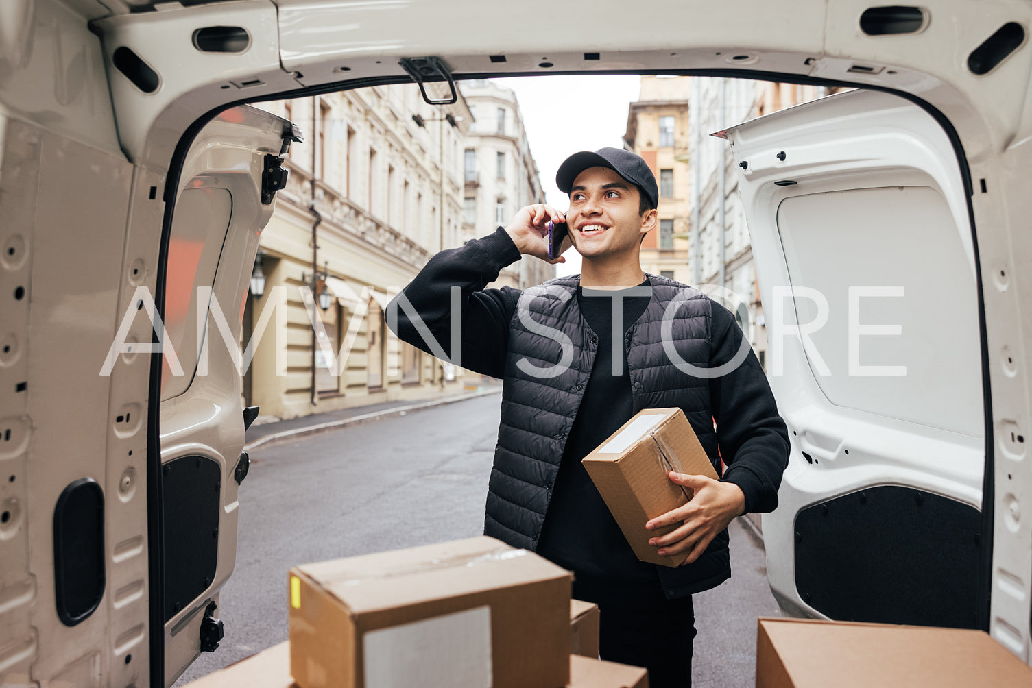 Smiling courier in uniform holding box and making call to a cust