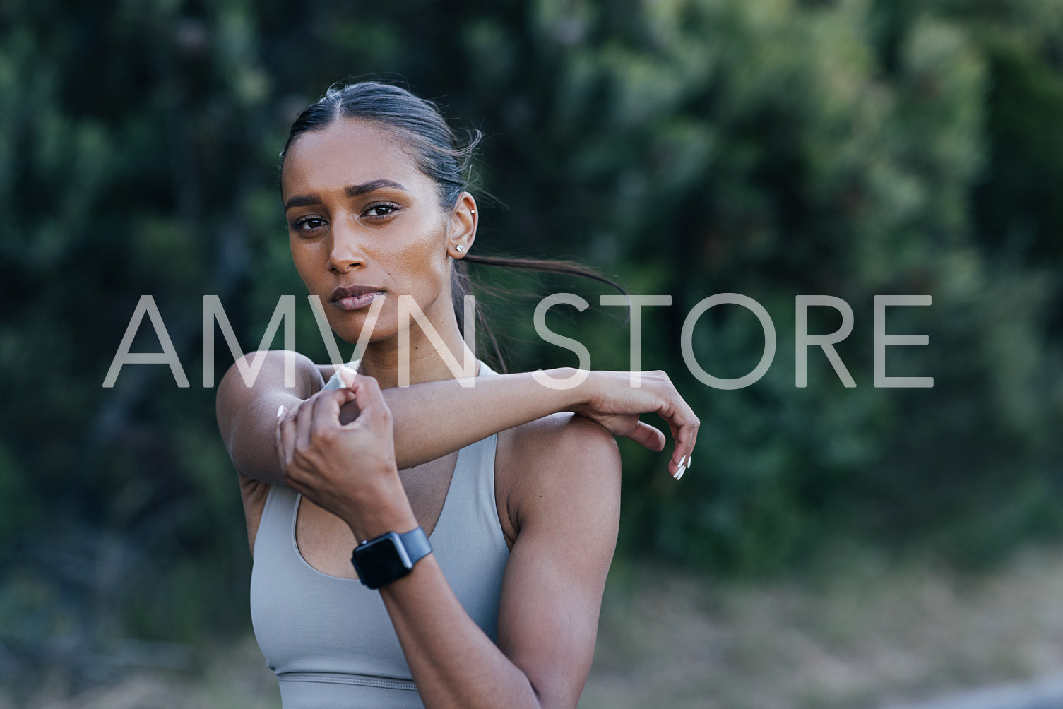 Slim woman stretching her arm and looking at camera. Confident sportswoman warming up a hand before an outdoor workout.