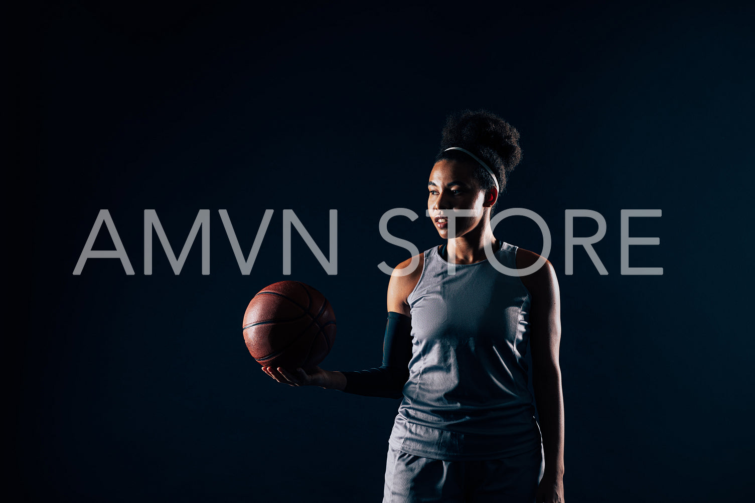 Young woman in team sportswear holding a basketball against a black backdrop