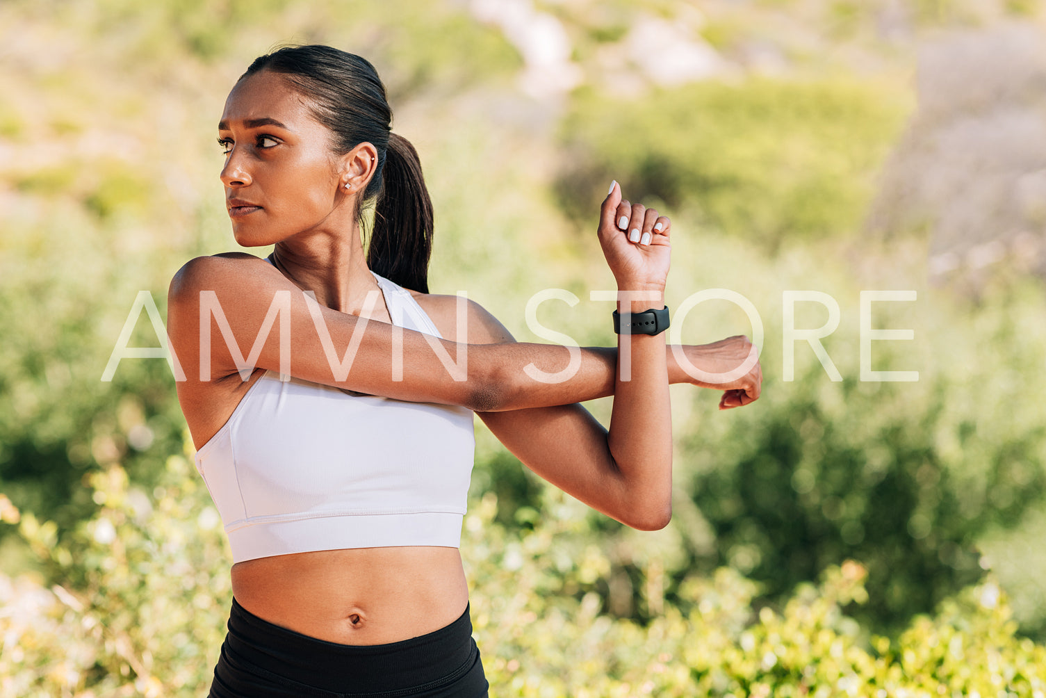 Slim and muscular female athlete flexing her hands and looking away. Young woman exercising outdoors on sunny day.