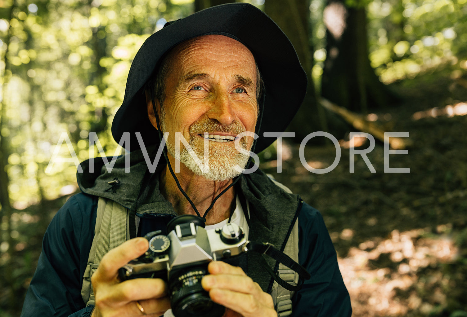 Portrait of a smiling male with a film camera. Senior man sitting in the forest and taking pictures on his film camera.