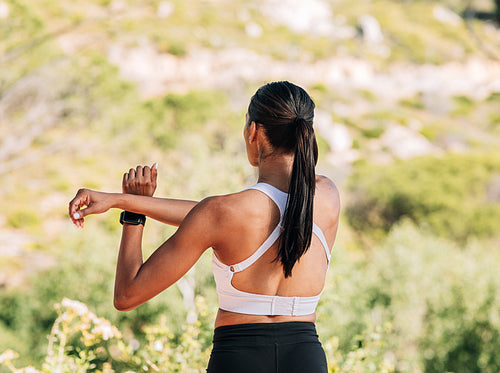 Rear view of slim woman athlete warming up upper body and hands while standing outdoors in natural park