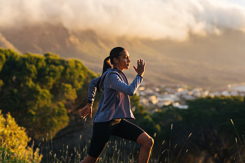 Young female running against mountains and clouds outdoors. Woman jogging outdoors with a stunning sunset in the background.