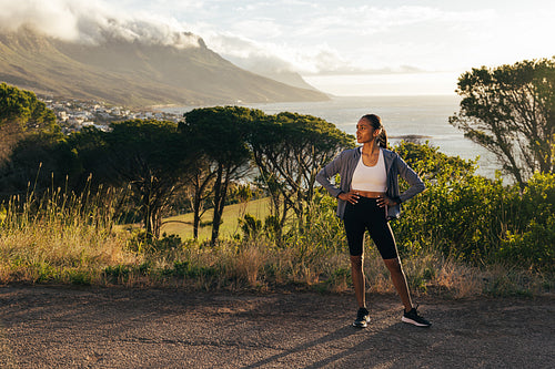 Confident female runner standing against a stunning view. Slim woman jogger relaxing during workout outdoors.