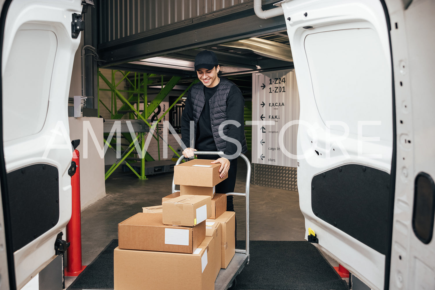 Smiling courier in uniform checking cardboard boxes on a cart wh