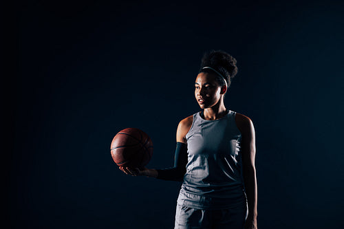 Young woman in team sportswear holding a basketball against a black backdrop