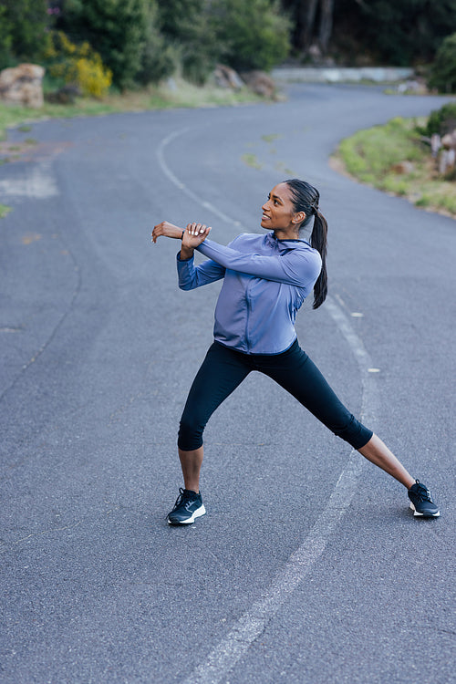 Young slim female warming up her body on an abandoned empty road