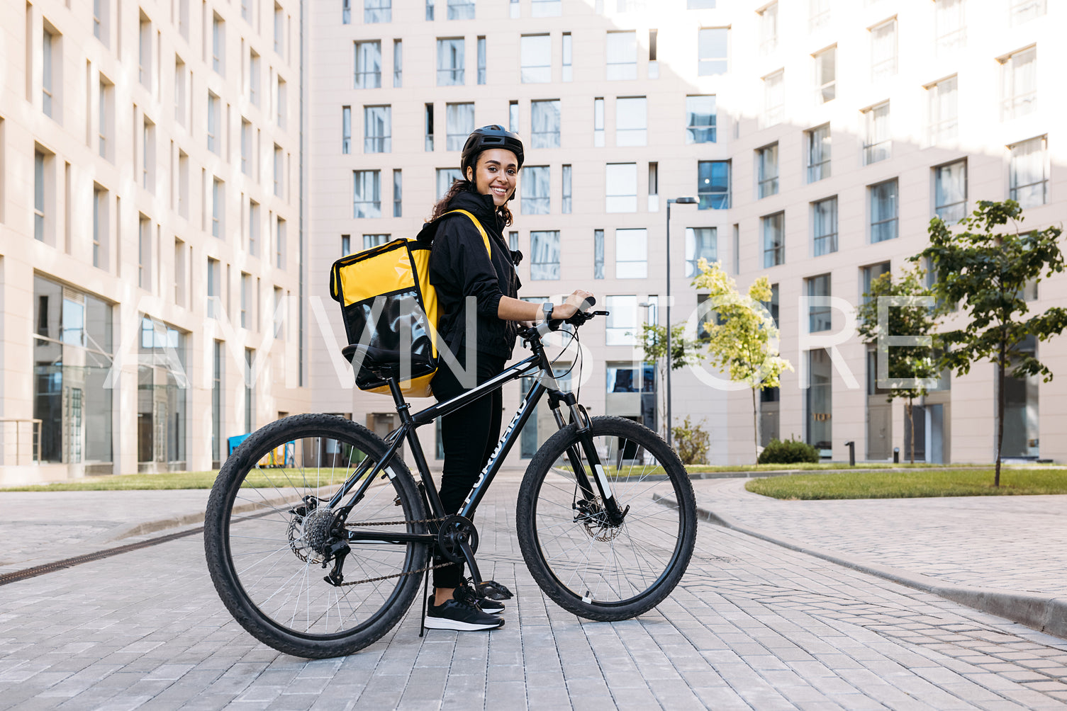 Smiling courier girl with bicycle, wearing a delivery thermal backpack looking at camera