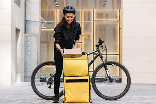 Smiling woman pulls a parcel out of her backpack while standing at an apartment building