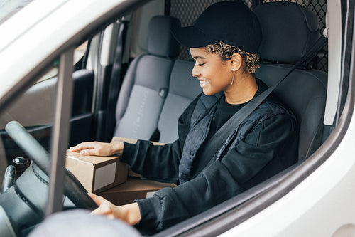 Smiling woman courier sitting on a driver seat checking boxes fo