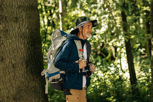 Senior male with backpack and hiking clothes walking in forest