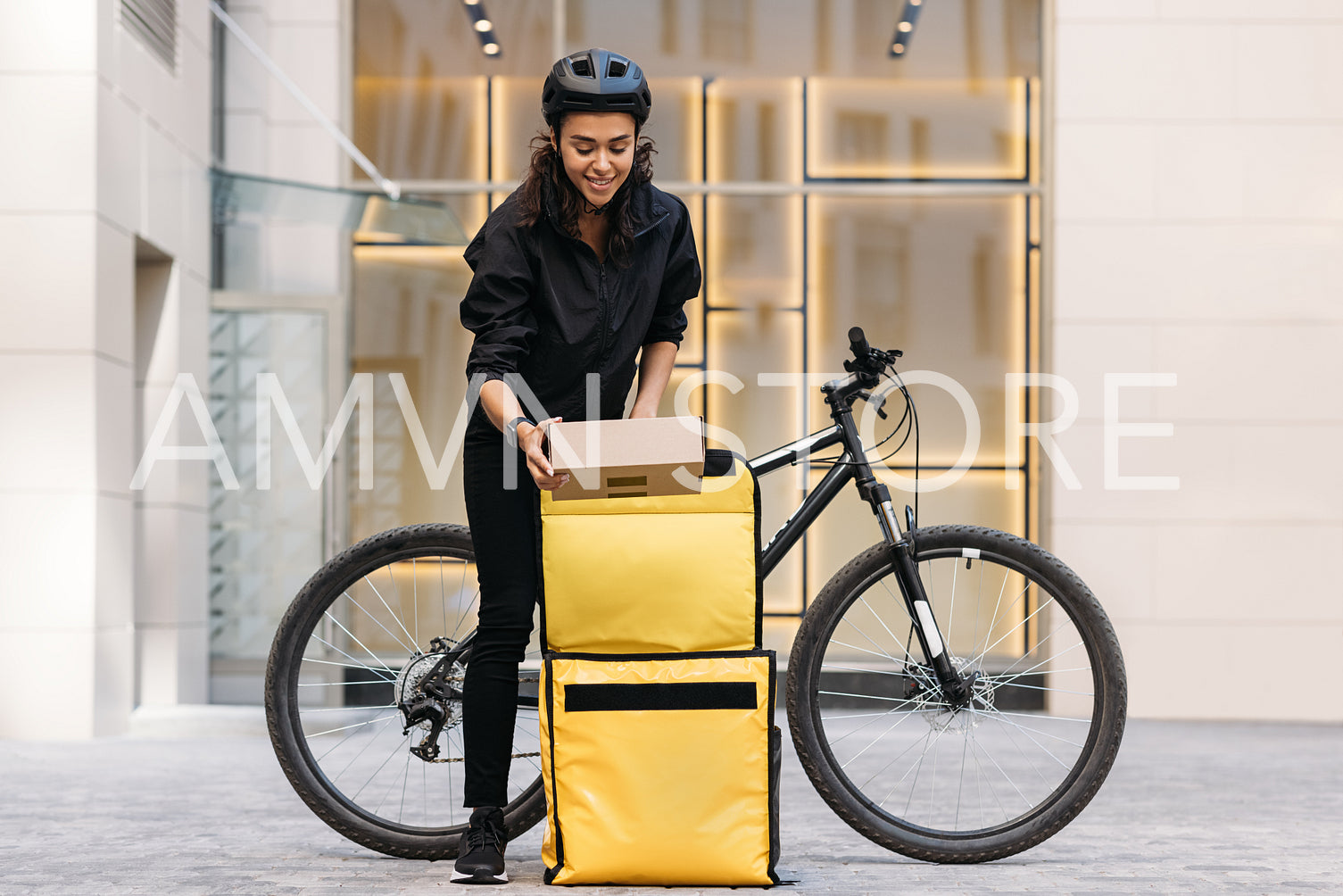 Smiling woman pulls a parcel out of her backpack while standing at an apartment building