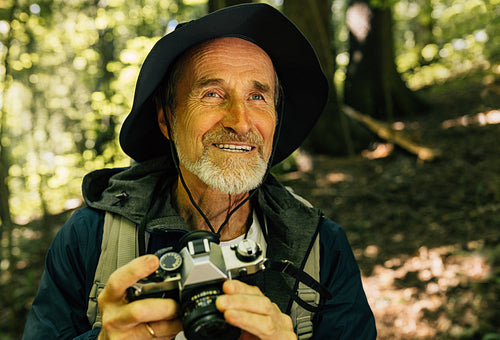 Portrait of a smiling male with a film camera. Senior man sitting in the forest and taking pictures on his film camera.