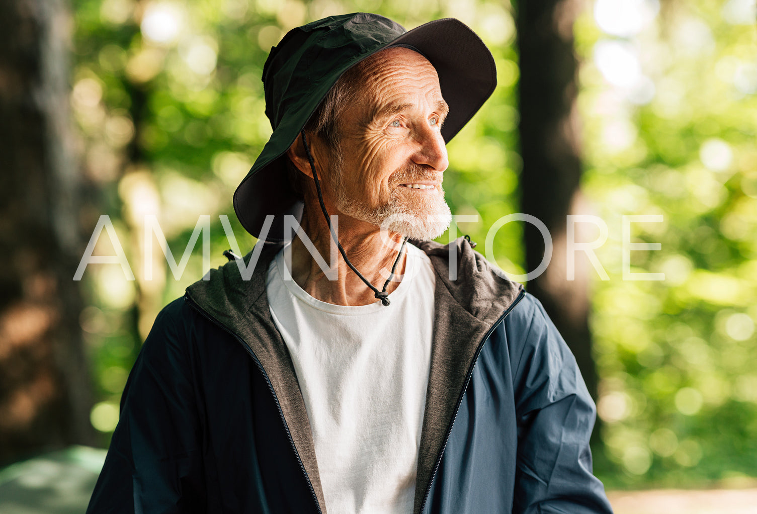 Portrait of a smiling senior tourist wearing a hat. Positive male tourist looking away while standing in a sunny forest.