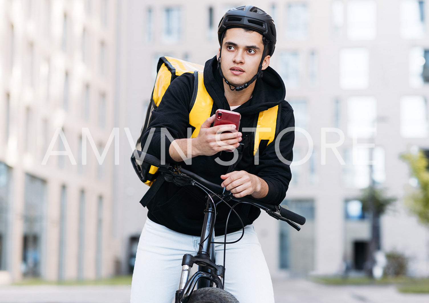 Portrait of young courier leaning on handlebar of a bike holding mobile phone looking for an address for delivery