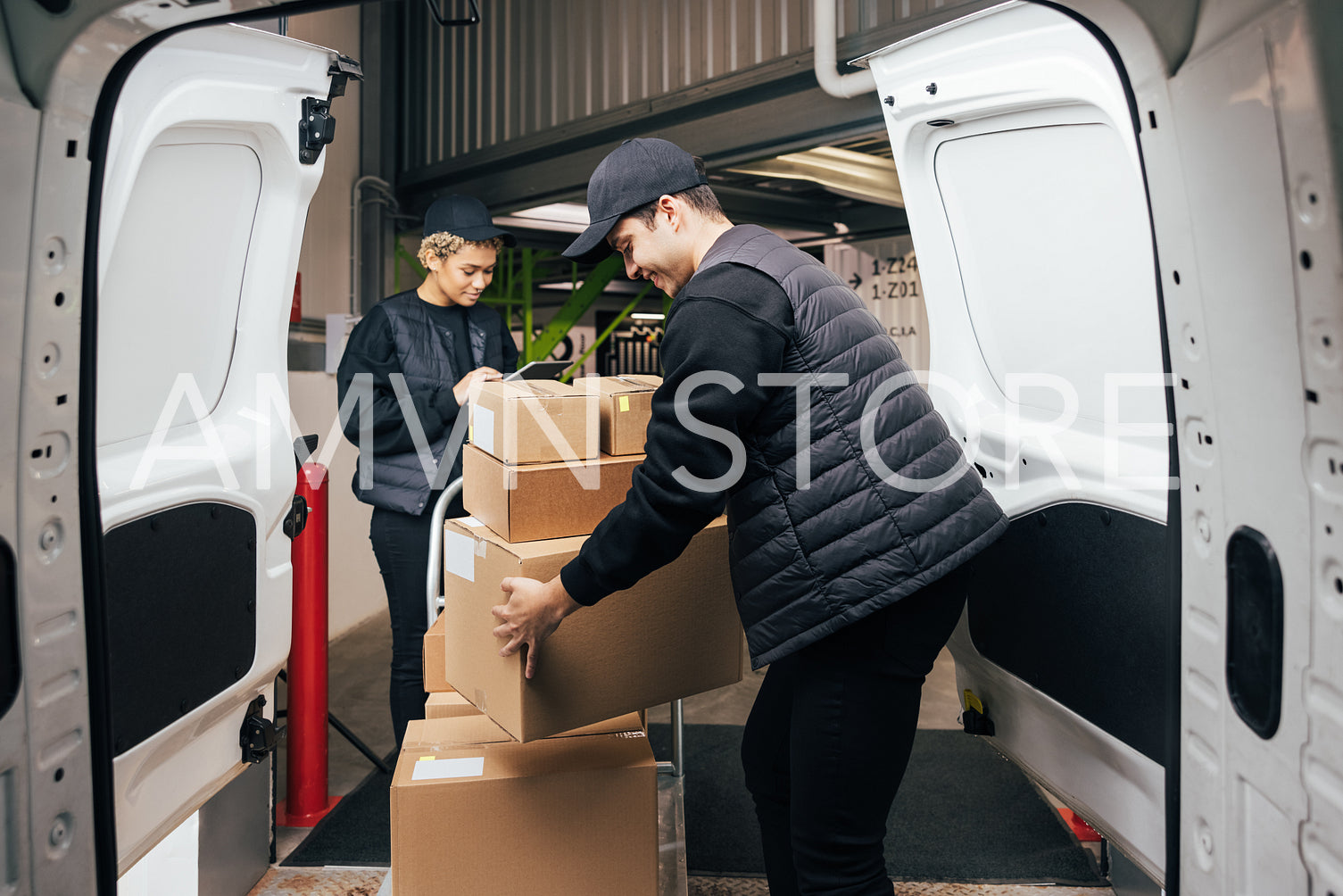 Side view male courier loads cardboard boxes from cart into the