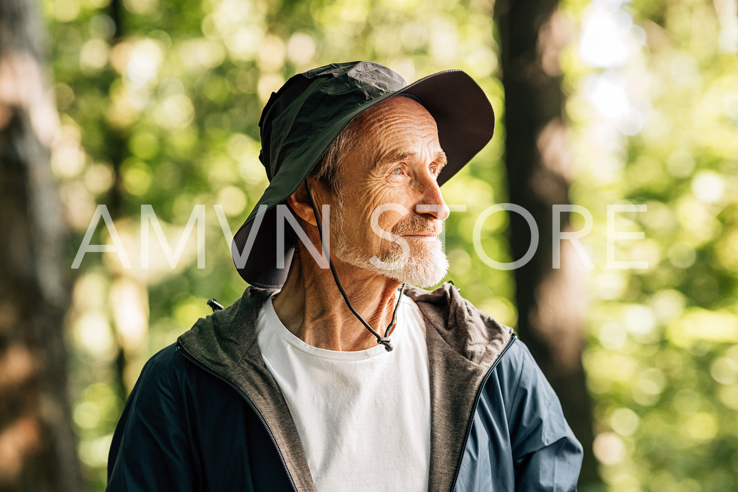 Side view of senior male in hat standing in forest. Portrait of a confident mature tourist posing outdoors.