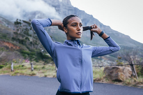 Young slim female in sportswear taking a break to adjust her hair during a run in a natural park