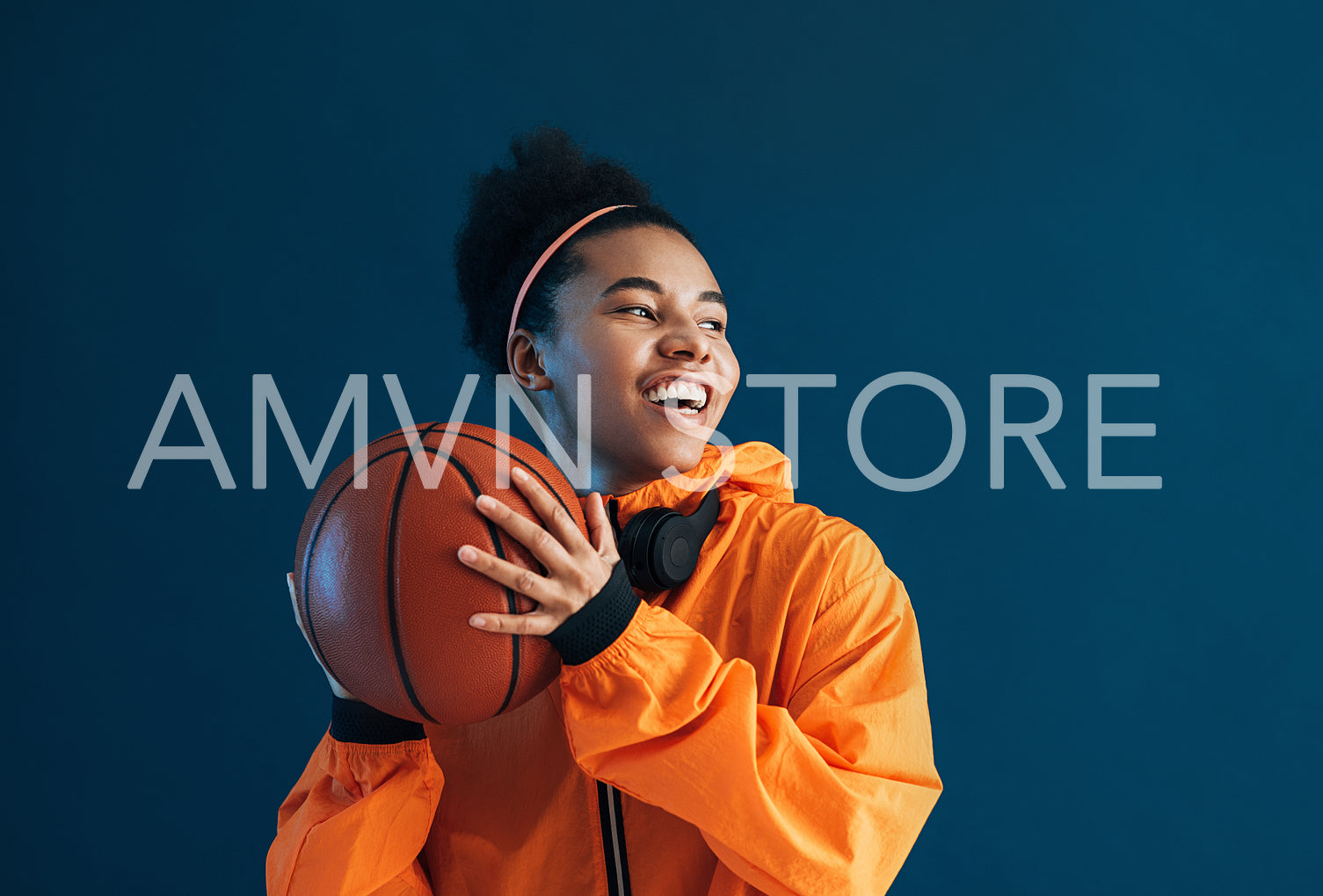 Happy professional basketball player holding basketball over blue backdrop in the studio and looking away