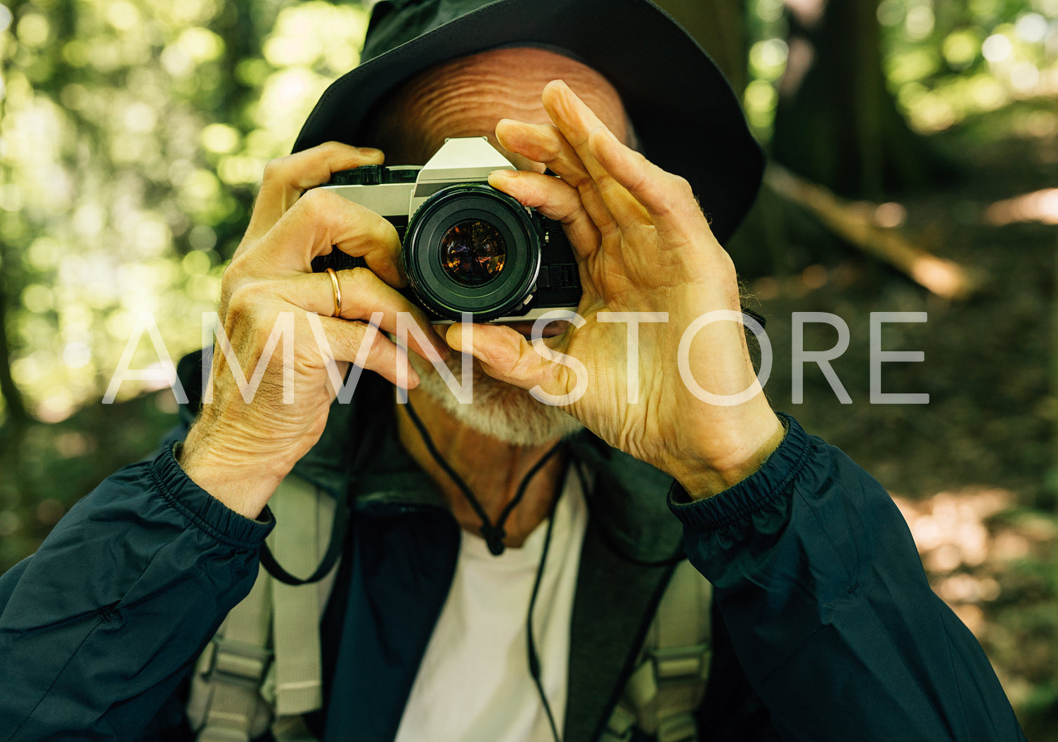 Close-up of a senior male in a hat taking pictures on a film camera. Mature man with a film camera in forest.