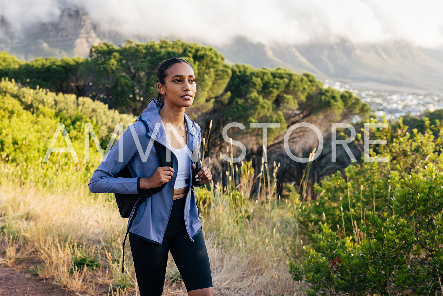 Woman with backpack and sportswear walking at sunset. Young female wearing fitness attire hiking in natural park.